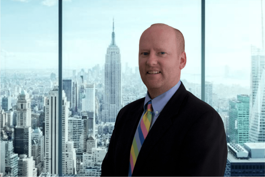 Kevin Owens, President and CEO, standing in front of window with city skyline in background