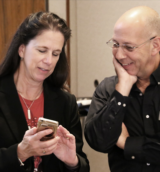 Smiling woman shows laughing man something on her cellphone