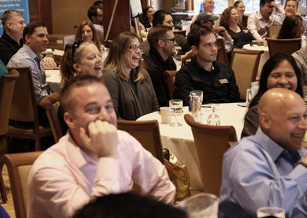 Crowd of laughing NYSTEC employees sitting at round tables at an event