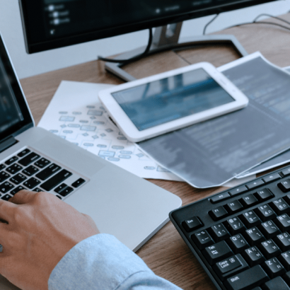 Information Systems Security Analyst image: a person's hands are on two keyboards atop a cluttered desk.